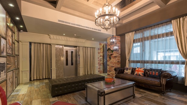 A spacious living room with a leather sofa, a red armchair, and a glass coffee table. A chandelier hangs from the ceiling, and there are curtains on the windows.