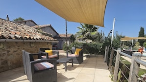 Un espace extérieur aménagé en terrasse, doté d’un sol carrelé, de meubles en osier et d’une grande voile d’ombrage.