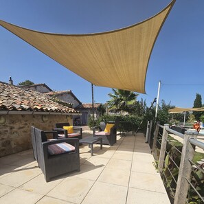Un espace extérieur aménagé en terrasse, doté d’un sol carrelé, de meubles en osier et d’une grande voile d’ombrage.