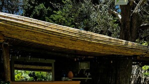 Un bar extérieur de style rustique, doté d’un comptoir en bois et de deux chaises blanches.