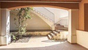 Un patio interior con una escalera que conduce a un nivel superior, rodeado de muros y un suelo de baldosas.