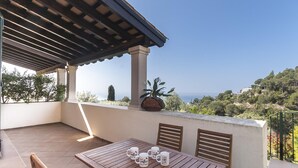 Un patio con una mesa y sillas de madera, una planta en maceta y vistas al mar.