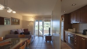 Una cocina moderna con armarios de madera, un comedor con mesa y sillas, y una sala de estar con sofá y televisor.