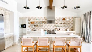 Una cocina moderna con una isla central, sillas de madera, luces colgantes y un salpicadero con diseño.