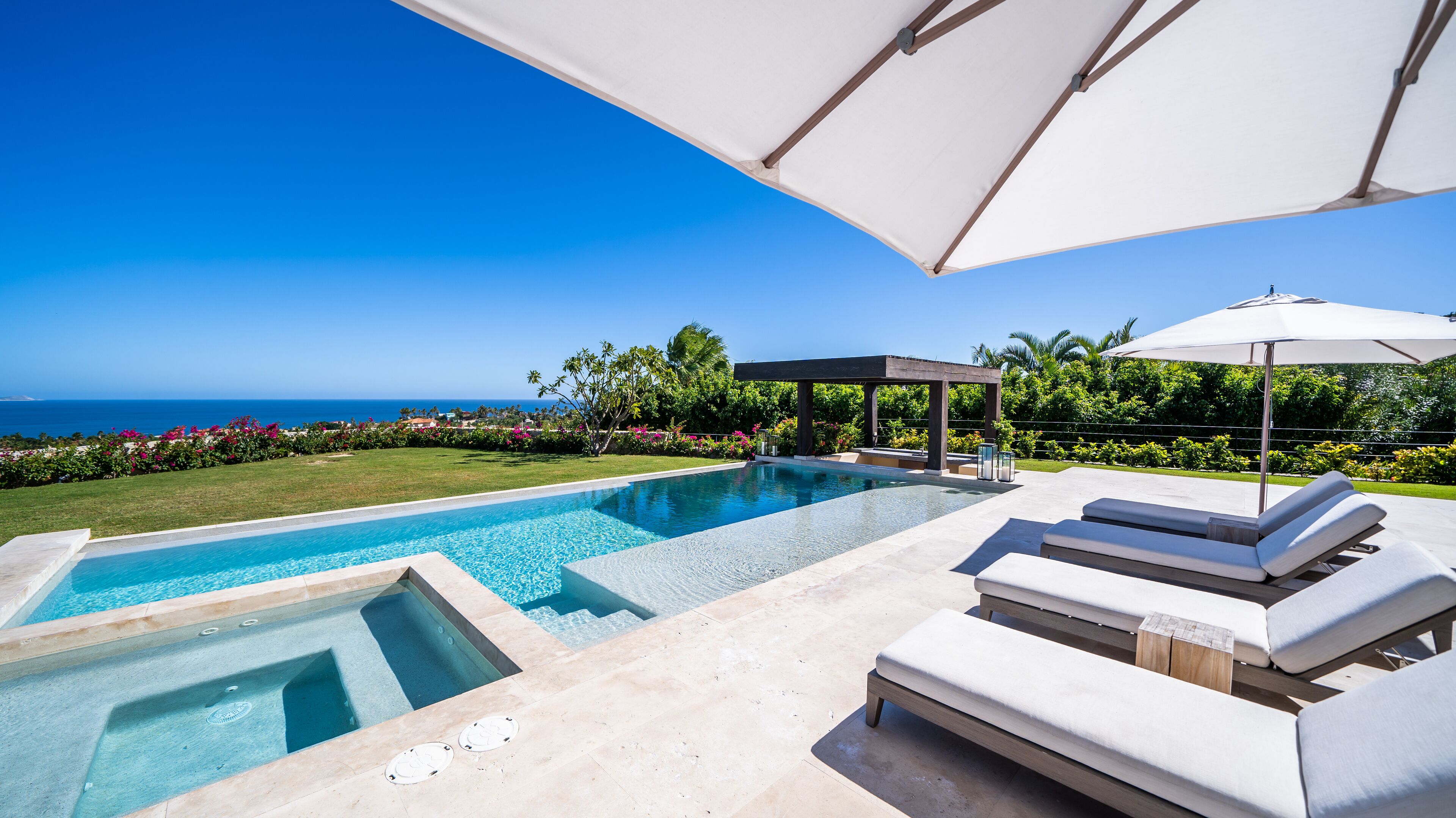 Ein Pool mit Meerblick, Liegestühlen und einem überdachten Bereich.
