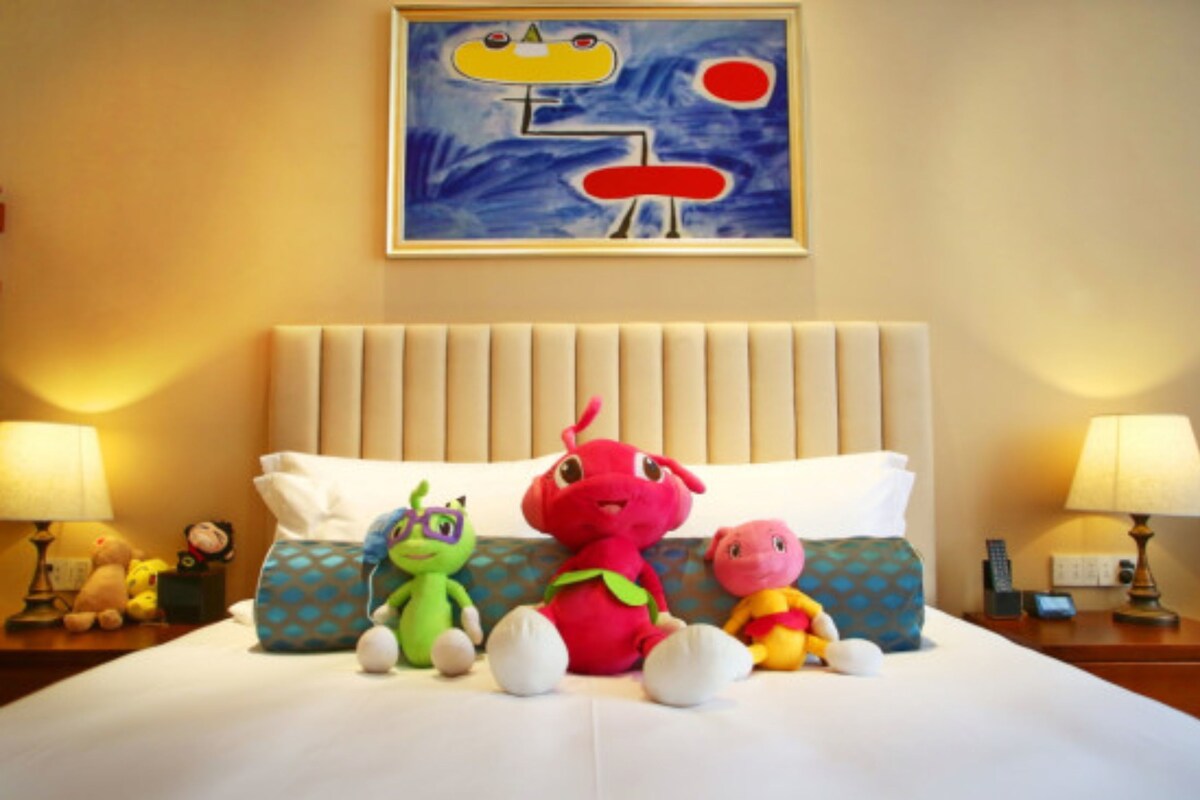 Une chambre d’hôtel avec un grand lit, des peluches, un tableau au mur et des lampes de chevet.