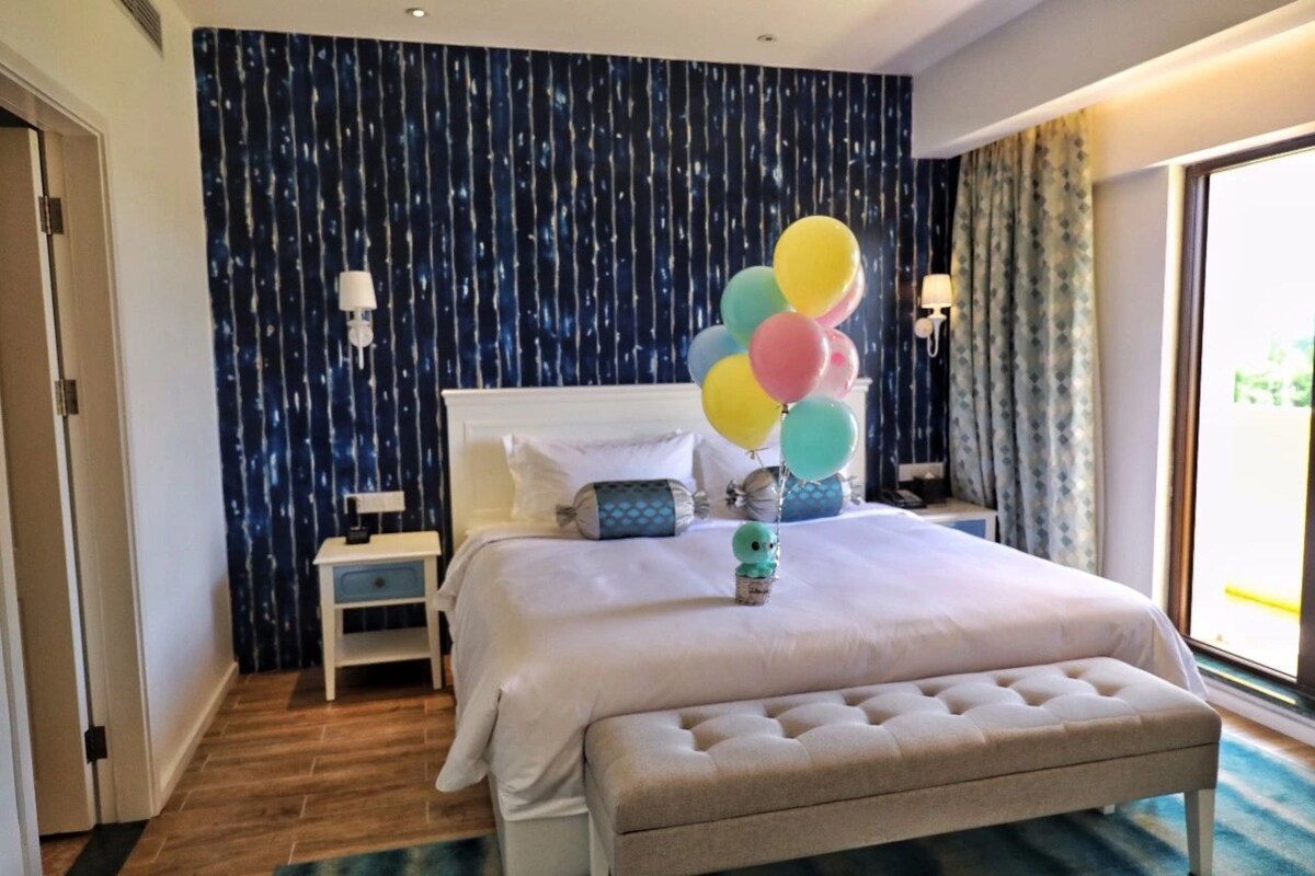Une chambre d’hôtel avec un grand lit, une table de chevet, un banc et une vue sur l’extérieur.
