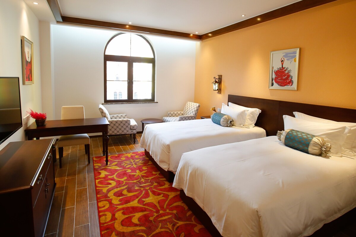 Une chambre d’hôtel avec deux lits, un bureau, une chaise, une télévision et une grande fenêtre.