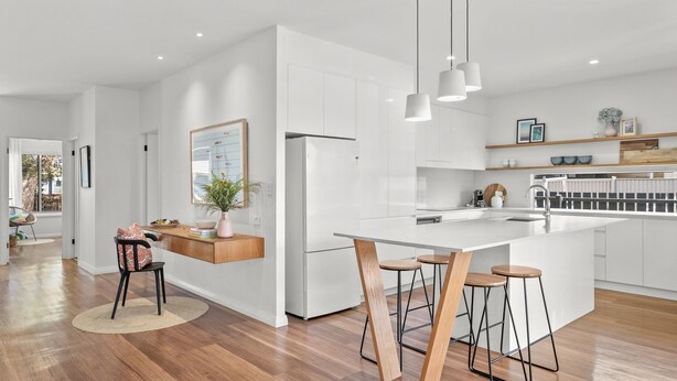 A modern kitchen with white cabinetry, a central island with bar stools, pendant lighting, and a view into the adjacent dining area.