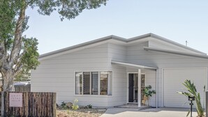 A modern two-story house with a garage, a covered entryway, and a small front yard with a wooden fence and a potted plant.