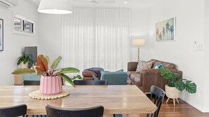Ein modernes Wohnzimmer mit einem Holzesstisch, einem braunen Ledersofa und einem großen Fenster mit transparenten Vorhängen.