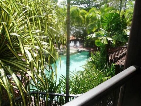 Relax by the serene pool surrounded by lush tropical plants and a traditional thatched-roof structure.