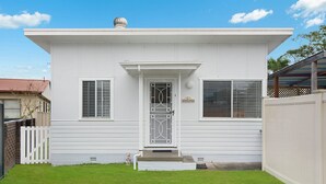 Una casa blanca de un piso con puerta principal, dos ventanas con contraventanas, un porche pequeño y un letrero que dice "Riverside".