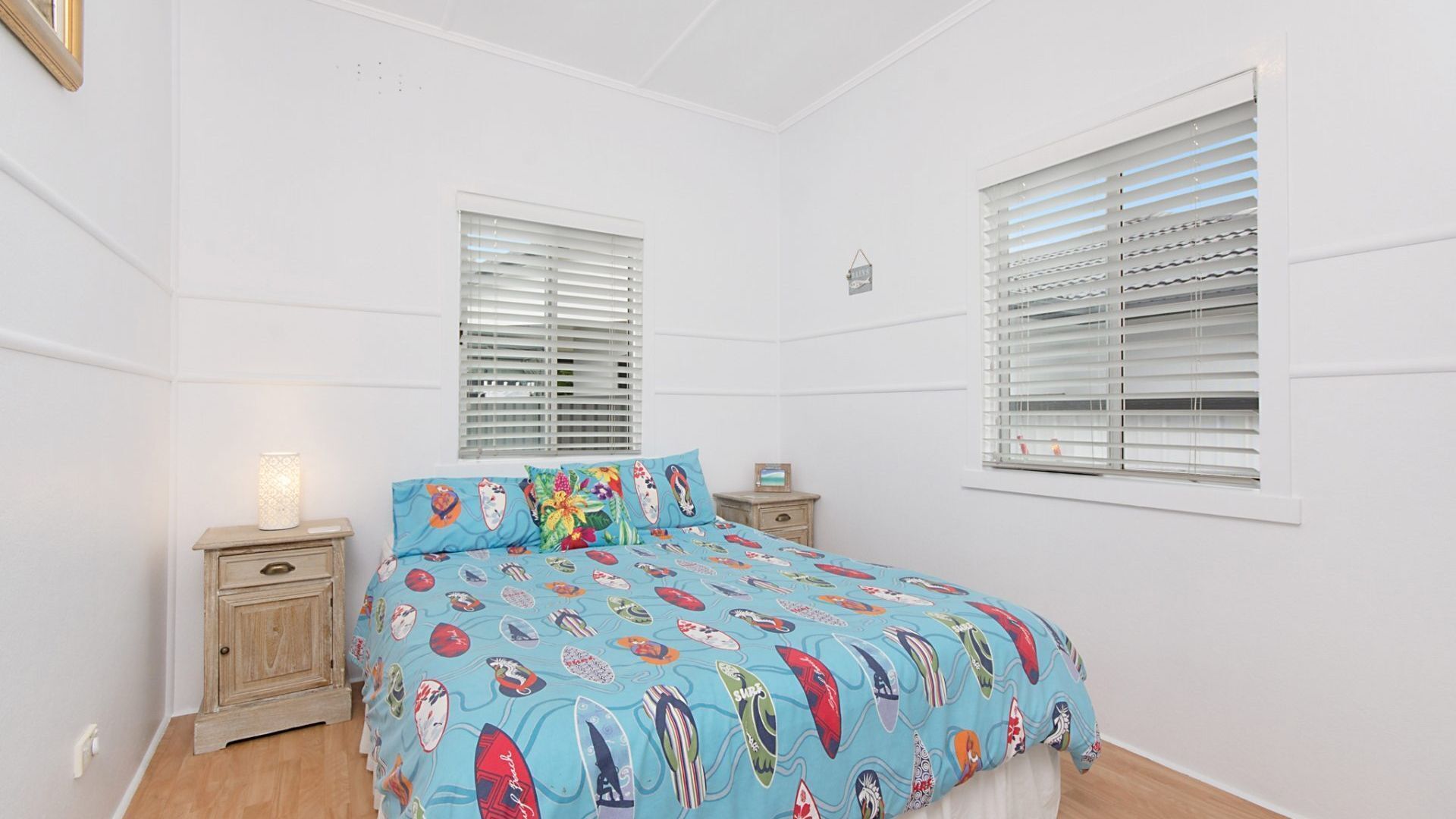 A bedroom with a bed, two nightstands, a lamp, and two windows with blinds.