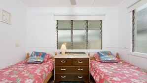 Un dormitorio con dos camas individuales, un aparador, una ventana con vidrio esmerilado y un ventilador de techo.