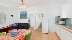 Un espacio habitable compacto con kitchenette, una zona de comedor con mantel colorido, un sofá y vistas al mar a través de una ventana.