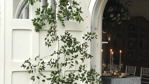 A white door with green foliage, an arched doorway, and a table set with candles and flowers. - Enjoy our 3-story, family-friendly Carriage House Fireplace and outdoor fire pit (West Redding)