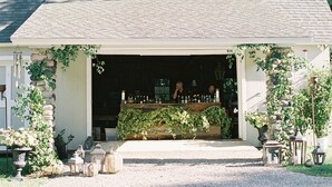 A covered outdoor area with a stone wall, a wooden bench, and potted plants. - Enjoy our 3-story, family-friendly Carriage House Fireplace and outdoor fire pit (West Redding)