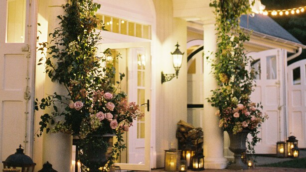 A house with a white facade, a dark roof, and a covered porch adorned with climbing plants and flowers. - Enjoy our 3-story, family-friendly Carriage House Fireplace and outdoor fire pit (West Redding)