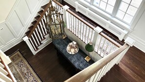 A staircase with a wooden handrail, a decorative lantern, and a marble-topped console table with a lamp. - Enjoy our 3-story, family-friendly Carriage House Fireplace and outdoor fire pit (West Redding)