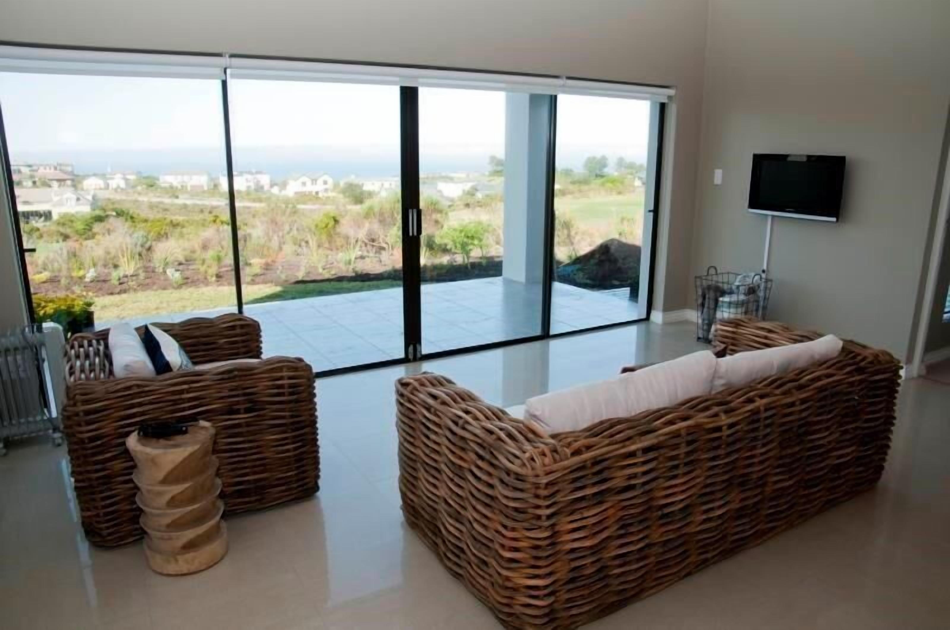 Een moderne woonkamer met rieten meubilair, een flatscreen televisie en een grote schuifglazen deur die leidt naar een balkon met uitzicht op zee.