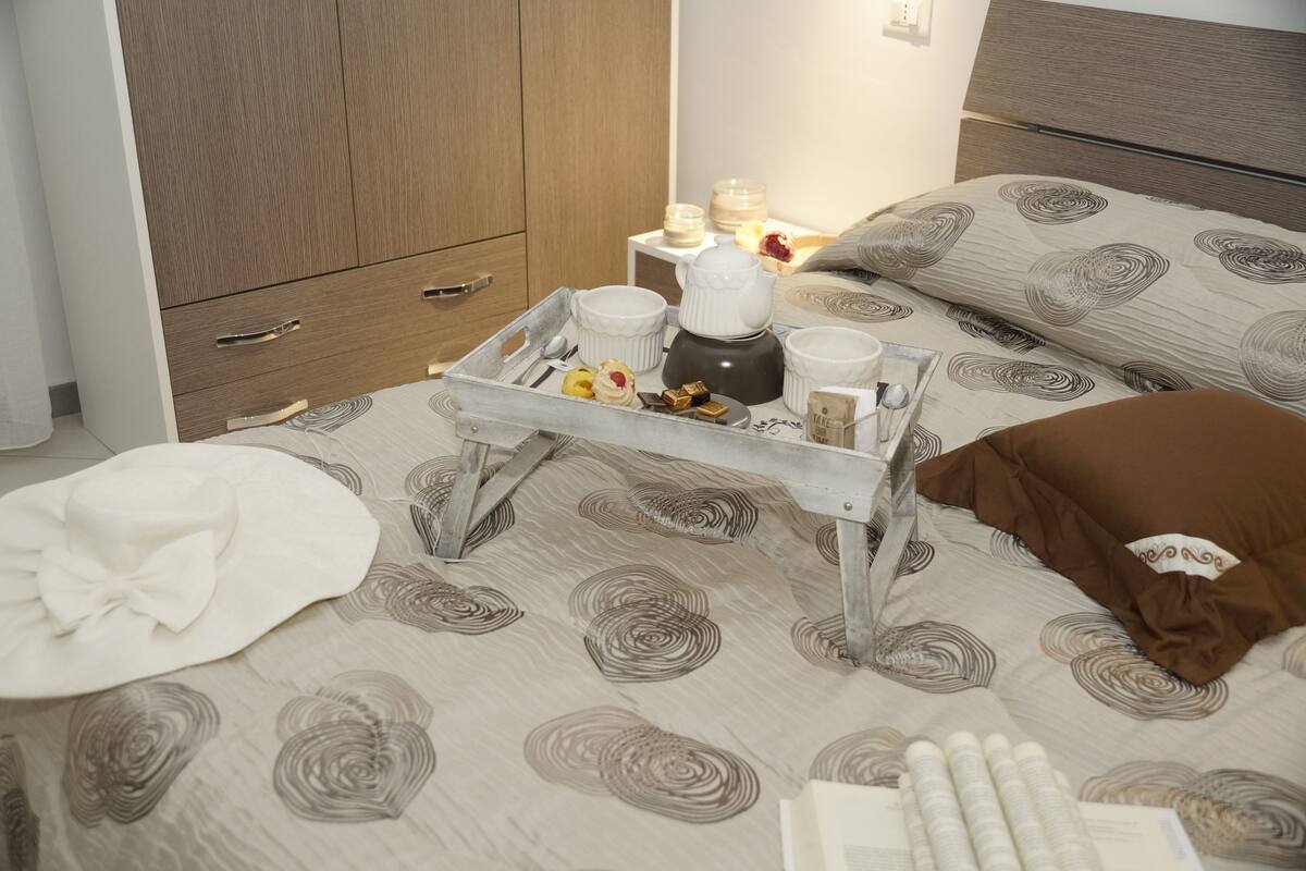 A neatly made bed with a tray of breakfast items, a bedside table with candles, and a wardrobe.