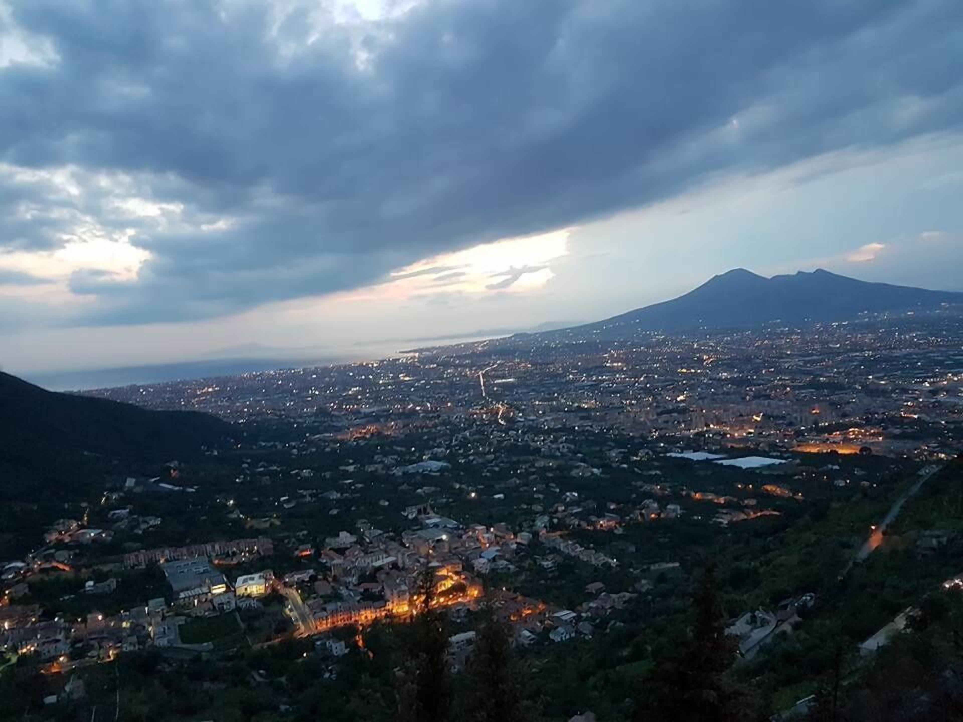 Un paisaje urbano con una montaña al fondo, luces brillantes de la ciudad y un cielo nublado.