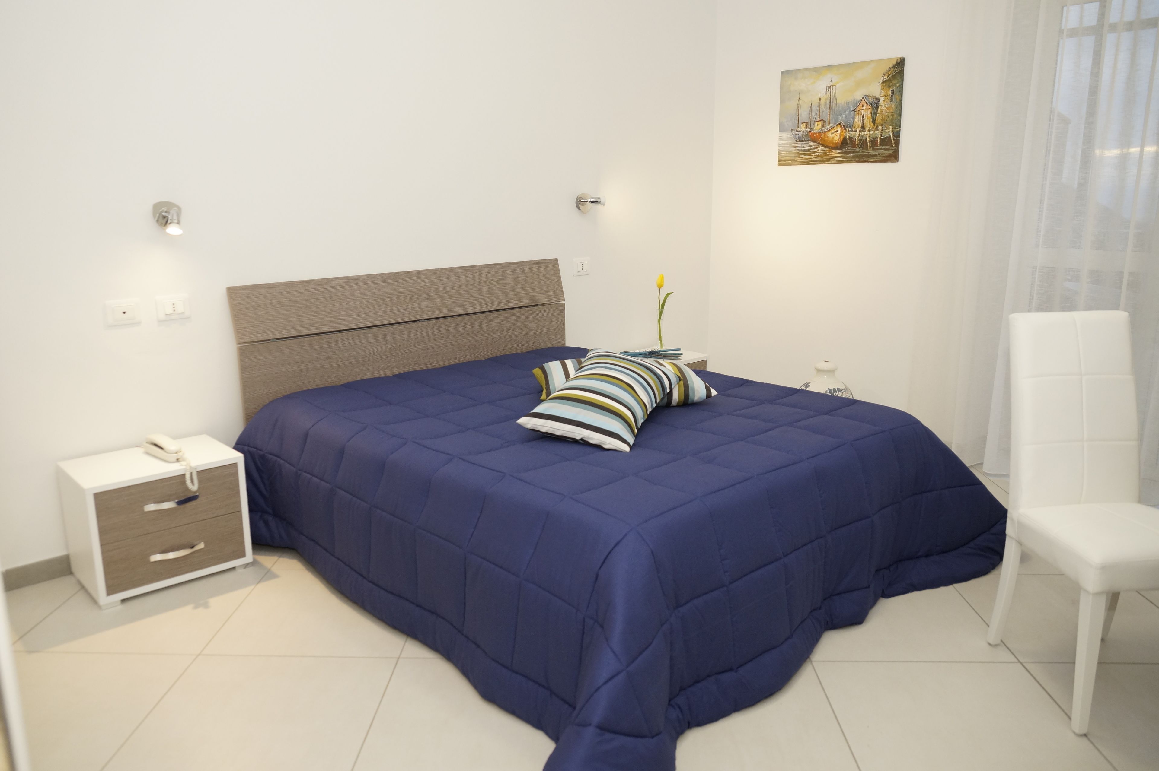 A bedroom with a large bed, a bedside table with a lamp, a chair, and a painting on the wall.