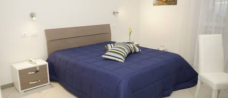 A bedroom with a large bed, a bedside table with a lamp, a chair, and a painting on the wall.