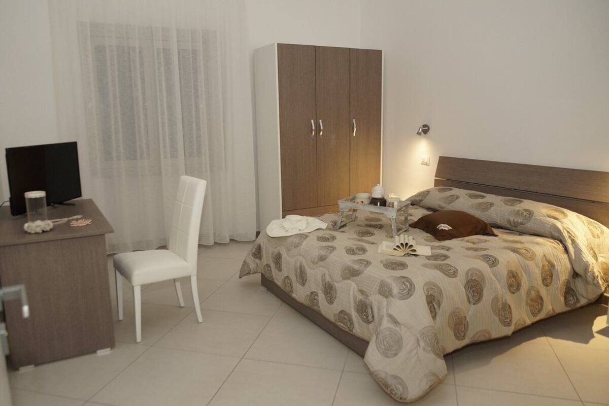 A hotel room with a bed, a desk, a chair, a wardrobe, and a television.