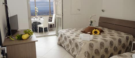 Un dormitorio con cama, escritorio, silla y vista de la ciudad a través de un ventanal.