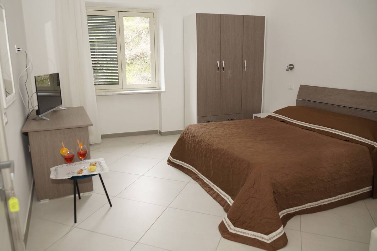 A bedroom with a bed, a desk with a computer, a wardrobe, and a window with blinds.