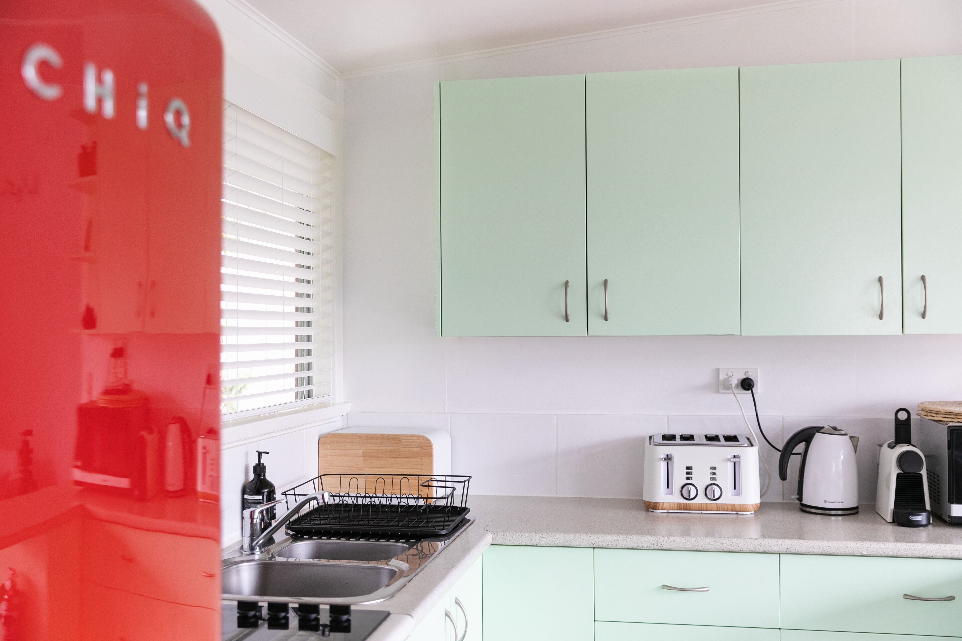 A kitchen with light green cabinets, a toaster, a kettle, and a sink.