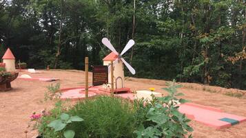 A windmill structure surrounded by a garden with various plants and a small building with a red roof.