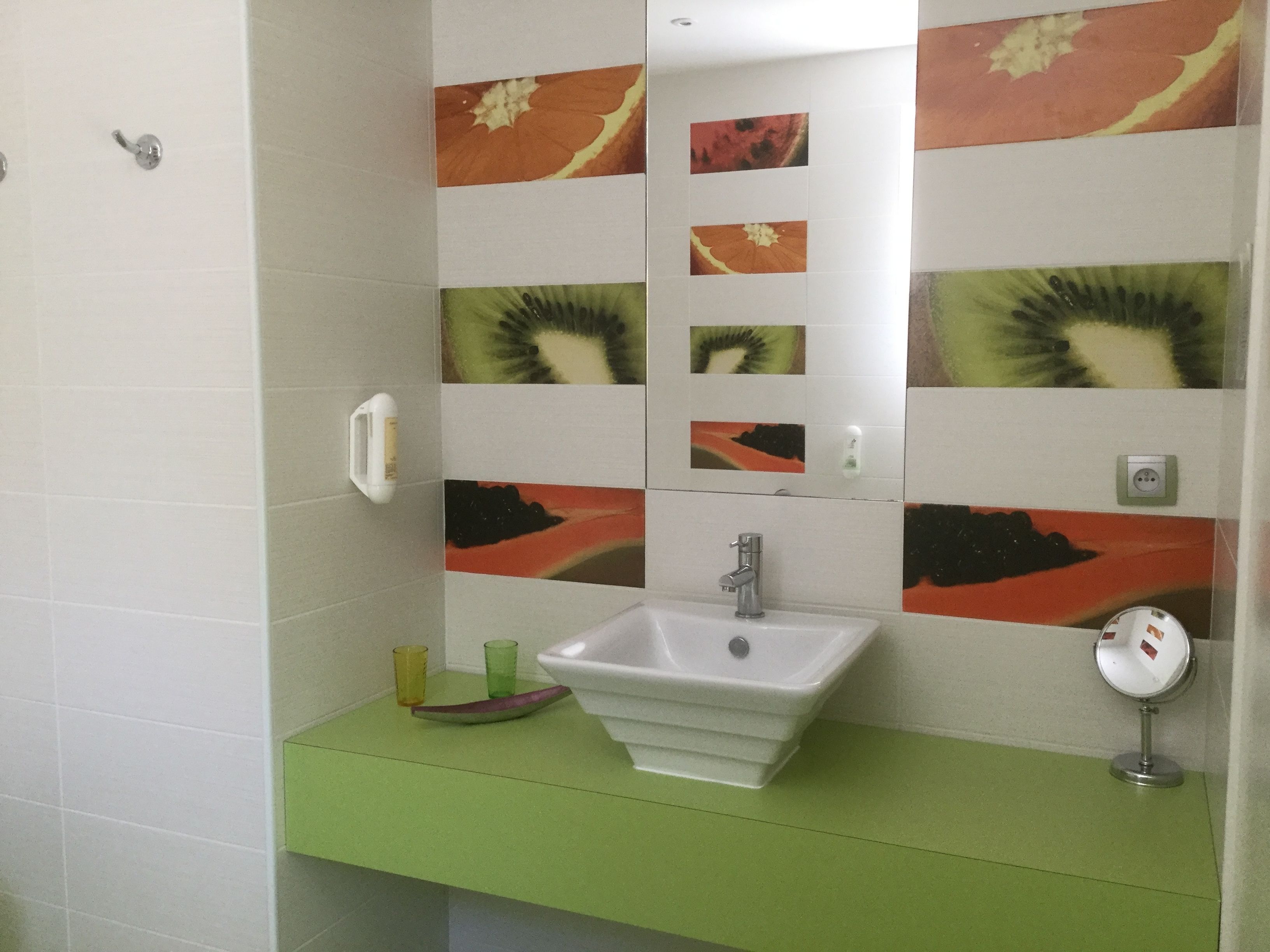 A bathroom with a white sink, green countertop, and decorative tiles featuring fruit and vegetable patterns.
