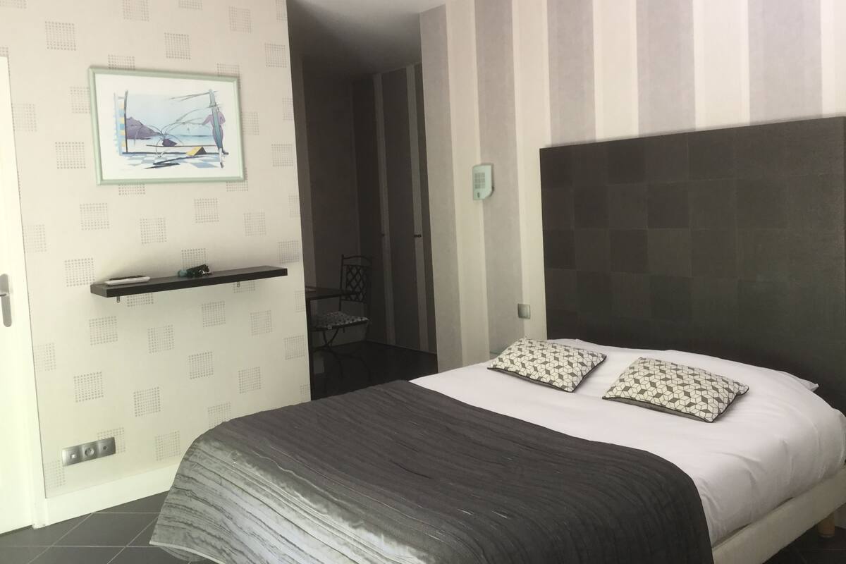 Une chambre moderne avec un grand lit, une tête de lit, une table de chevet, une chaise et une étagère fixée au mur.