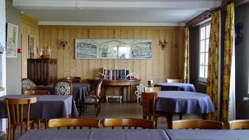 Un comedor con paredes de paneles de madera, una mesa central con libros y mesas con manteles azules.