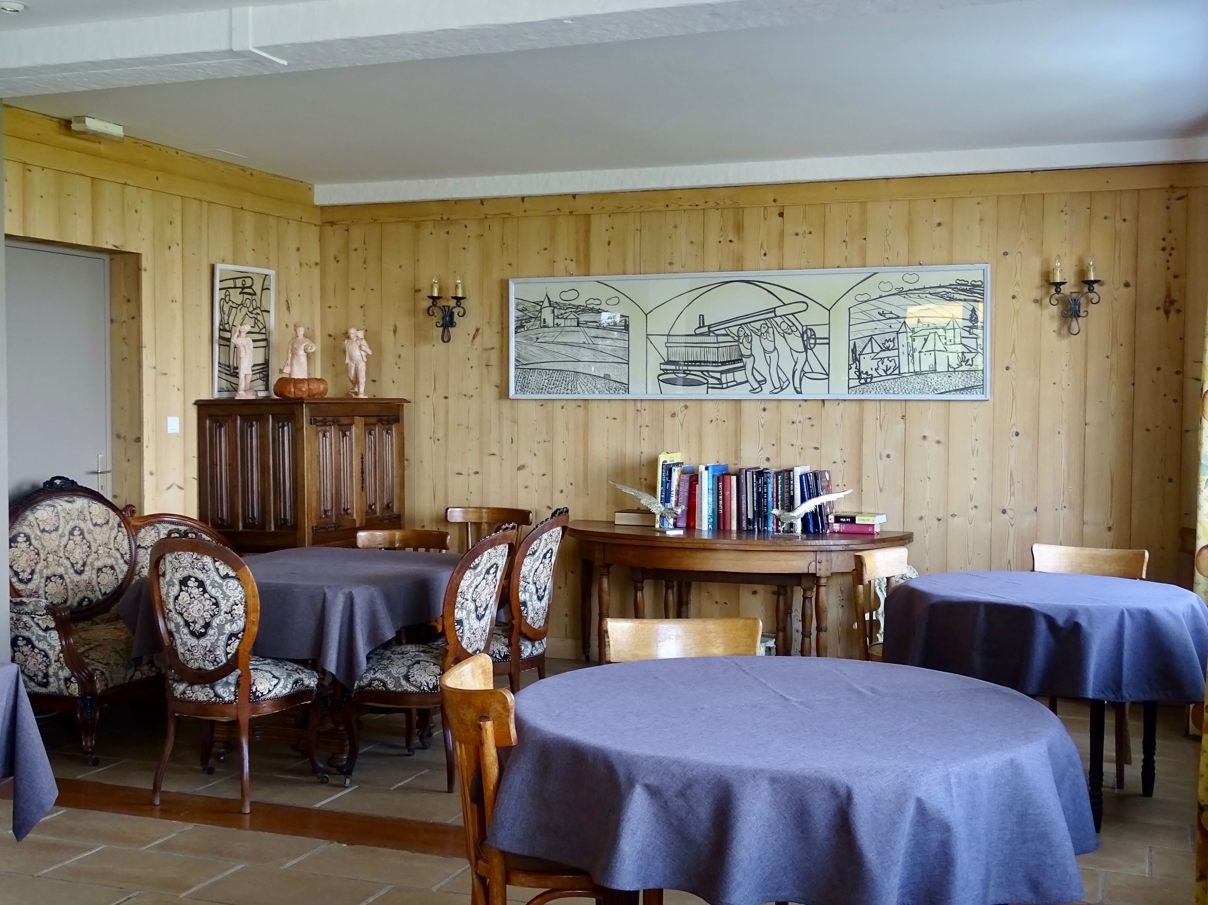 A dining area with wooden panel walls, a large mural, and a bookshelf.