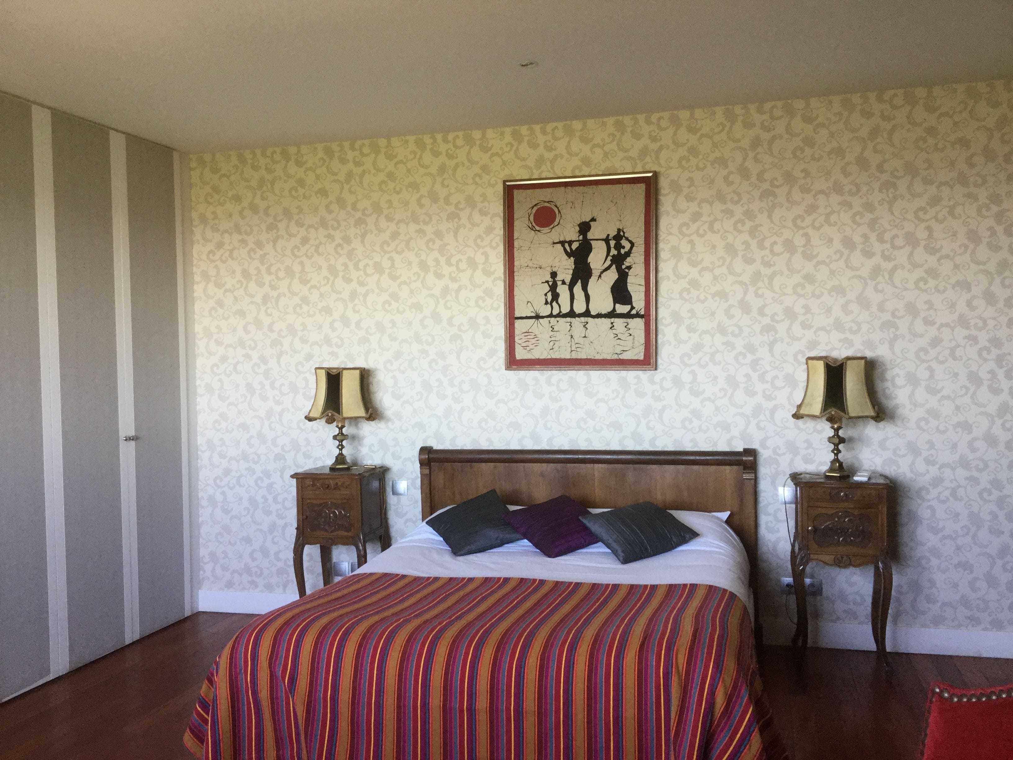 A bedroom with a striped bedspread, a wooden headboard, two bedside tables with lamps, and a wall-mounted picture.