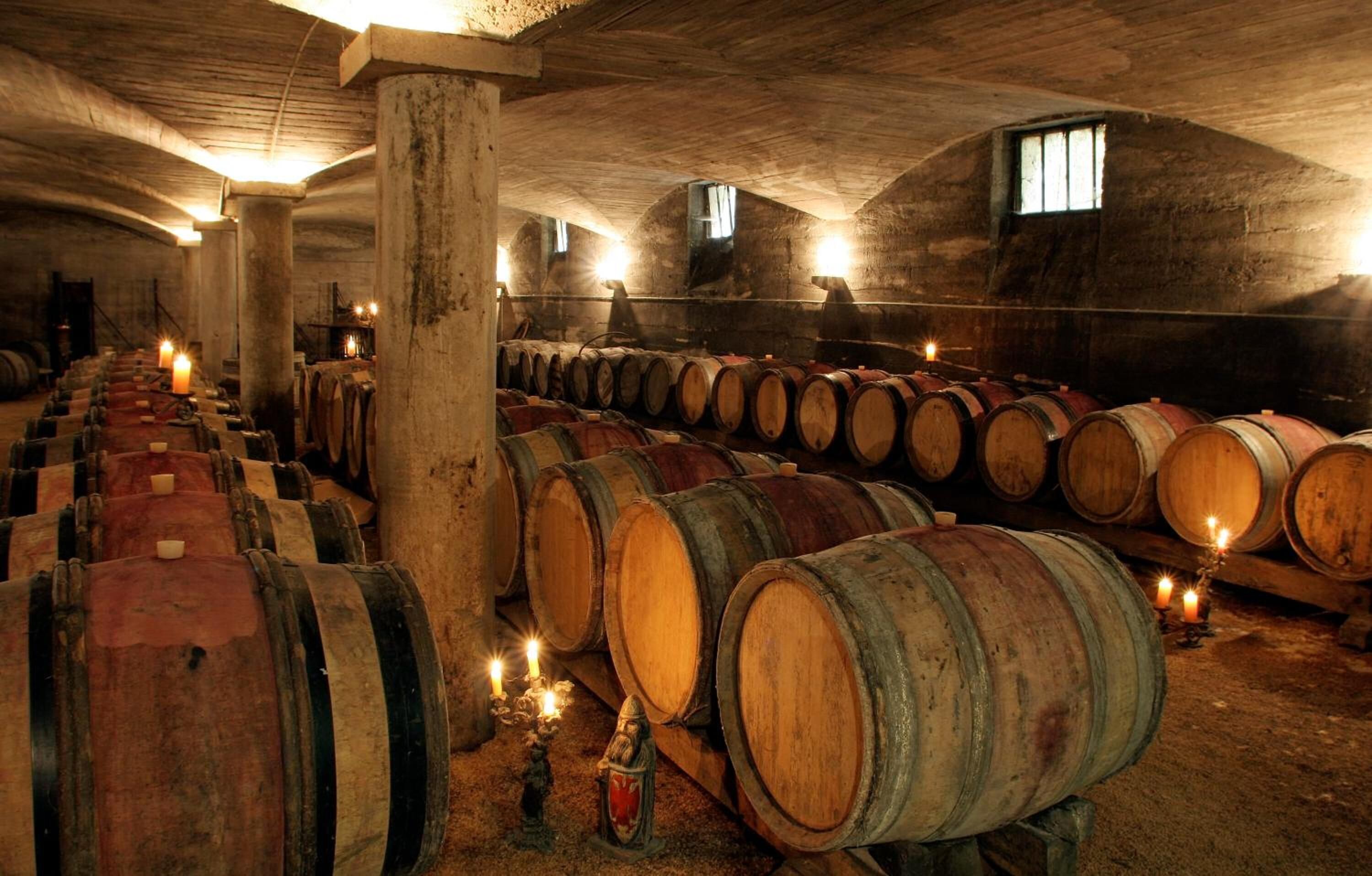 A cellar with wooden barrels arranged in rows, illuminated by candles.