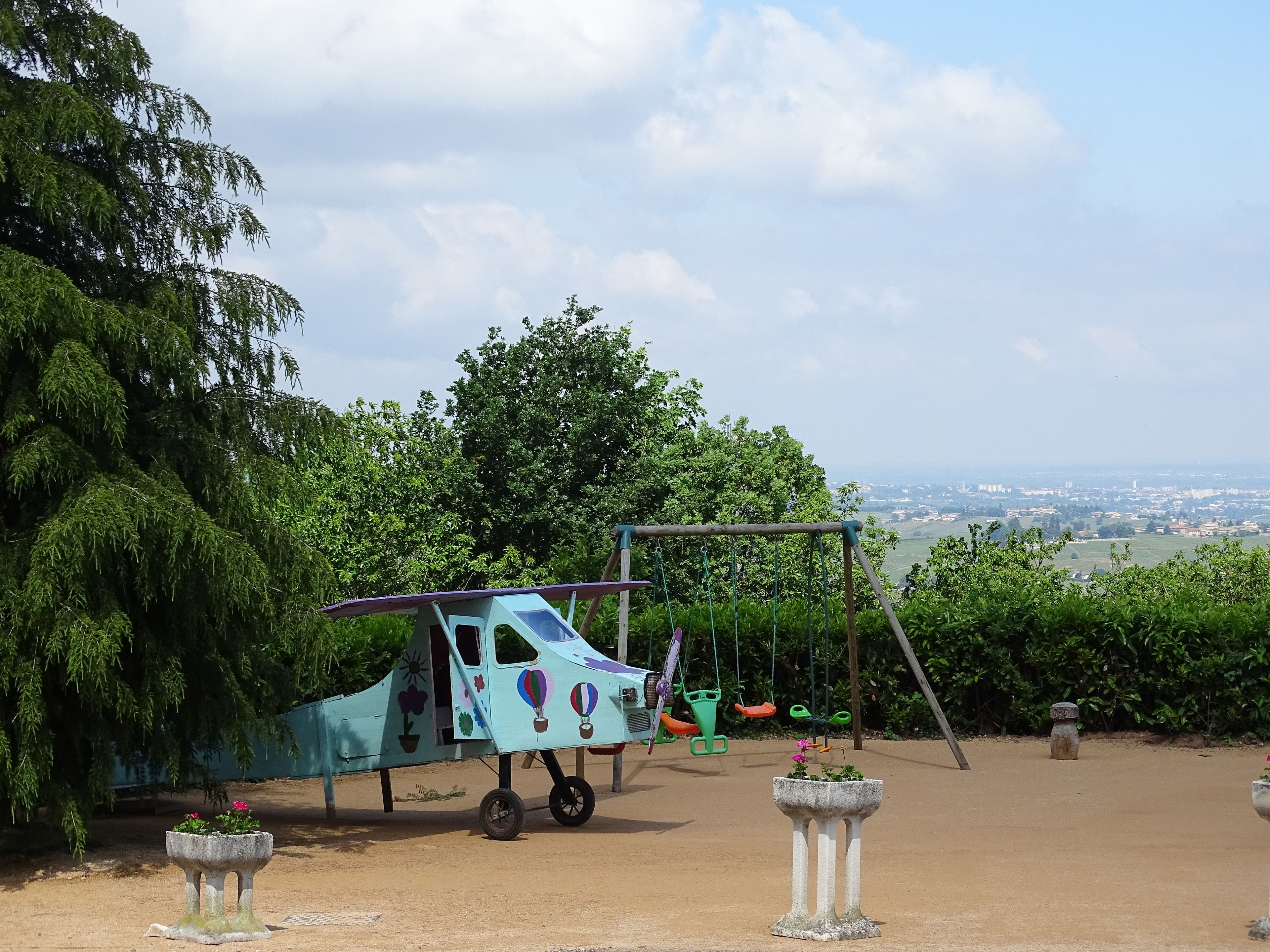 Ein Spielplatz mit Schaukeln und einem kleinen, blauen Spielhäuschen.