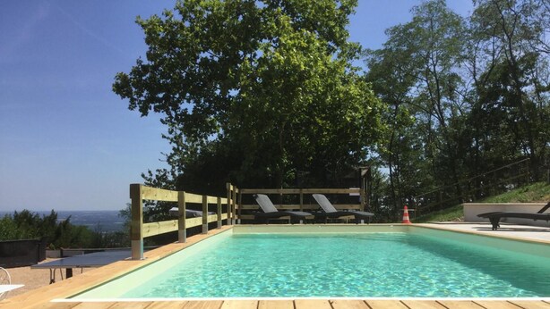 Una terraza de madera que conduce a una piscina cristalina con sillas de descanso y una valla de madera.