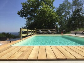 Una terraza de madera que conduce a una piscina cristalina con sillas de descanso y una valla de madera.