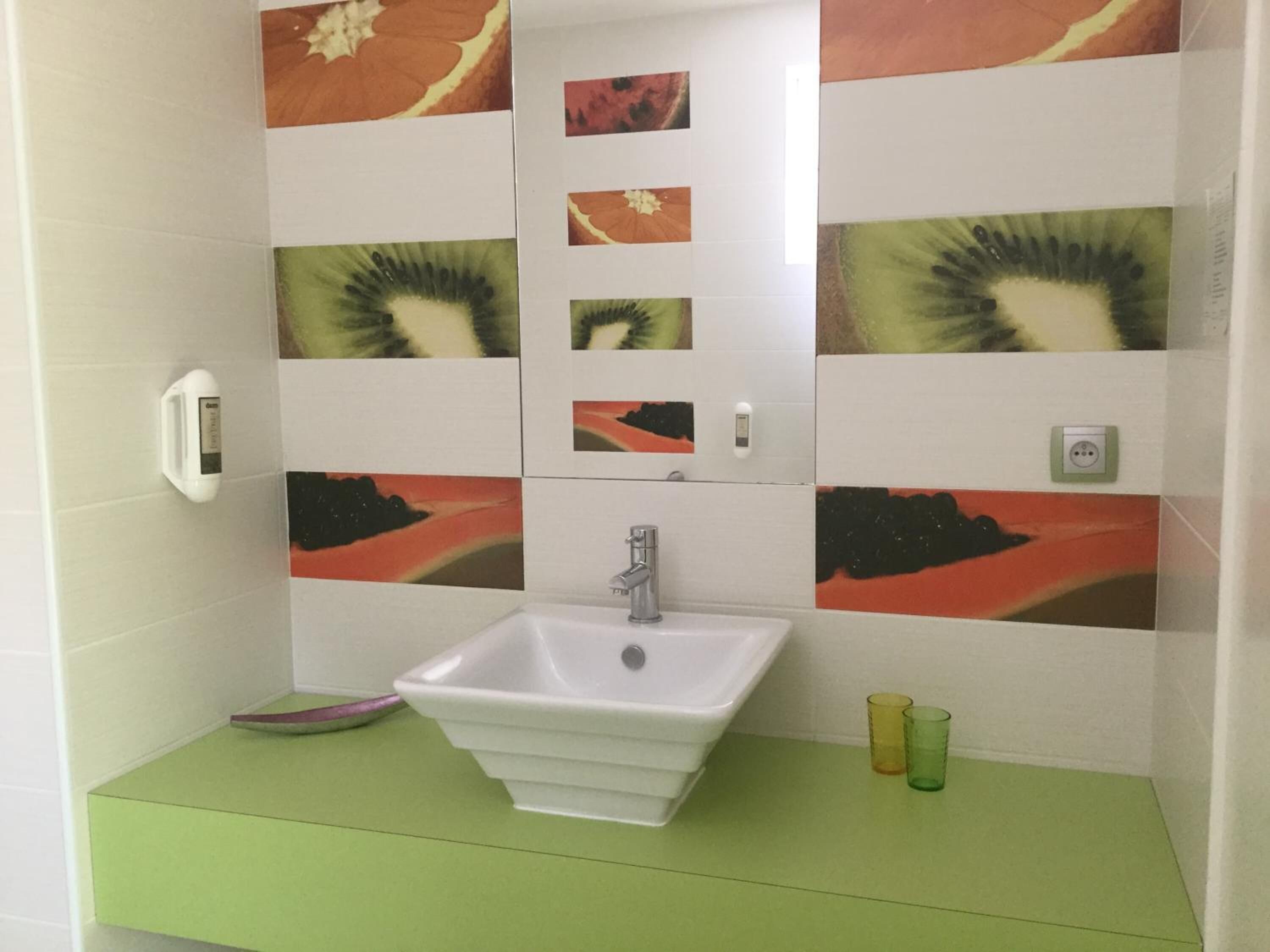 A bathroom with a white sink, green countertop, and decorative wall tiles.