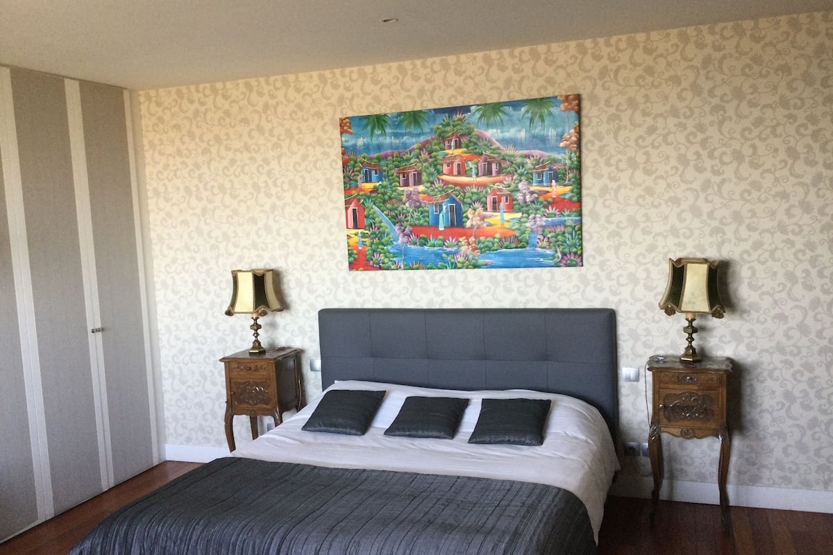 Une chambre à coucher avec un lit, deux tables de chevet, un tableau et un papier peint à motifs.