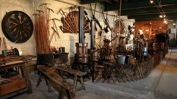 Un atelier rustique équipé de divers outils et matériels, notamment une grande scie circulaire, des établis en bois et des conteneurs métalliques.