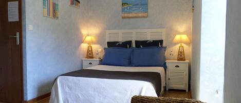 A bedroom with a bed, two bedside tables with lamps, a nightstand, a woven chair, and wall art.
