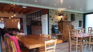 A spacious dining area with a large wooden table and chairs, a stone accent wall, and a coffee machine. - Chambres d'Hôtes La Rompardais (Pleven)