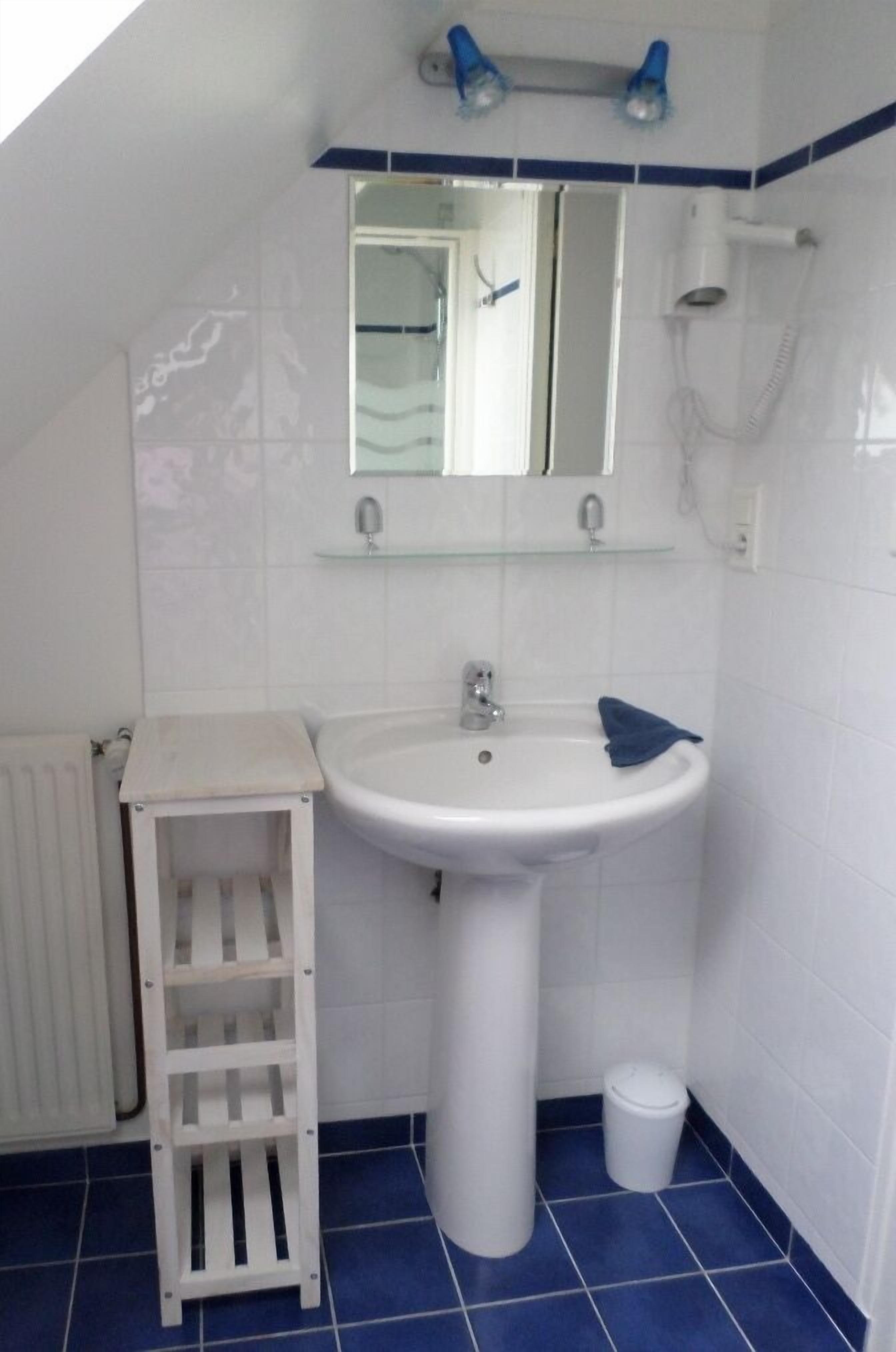 Ein Badezimmer mit einem weißen Waschbecken, einem Spiegel, einem Handtuch und einem kleinen Hocker.