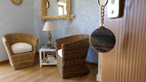 A room with two wicker chairs, a small table with a lamp, and a round sign with text. - Chambres d'Hôtes La Rompardais (Pleven)